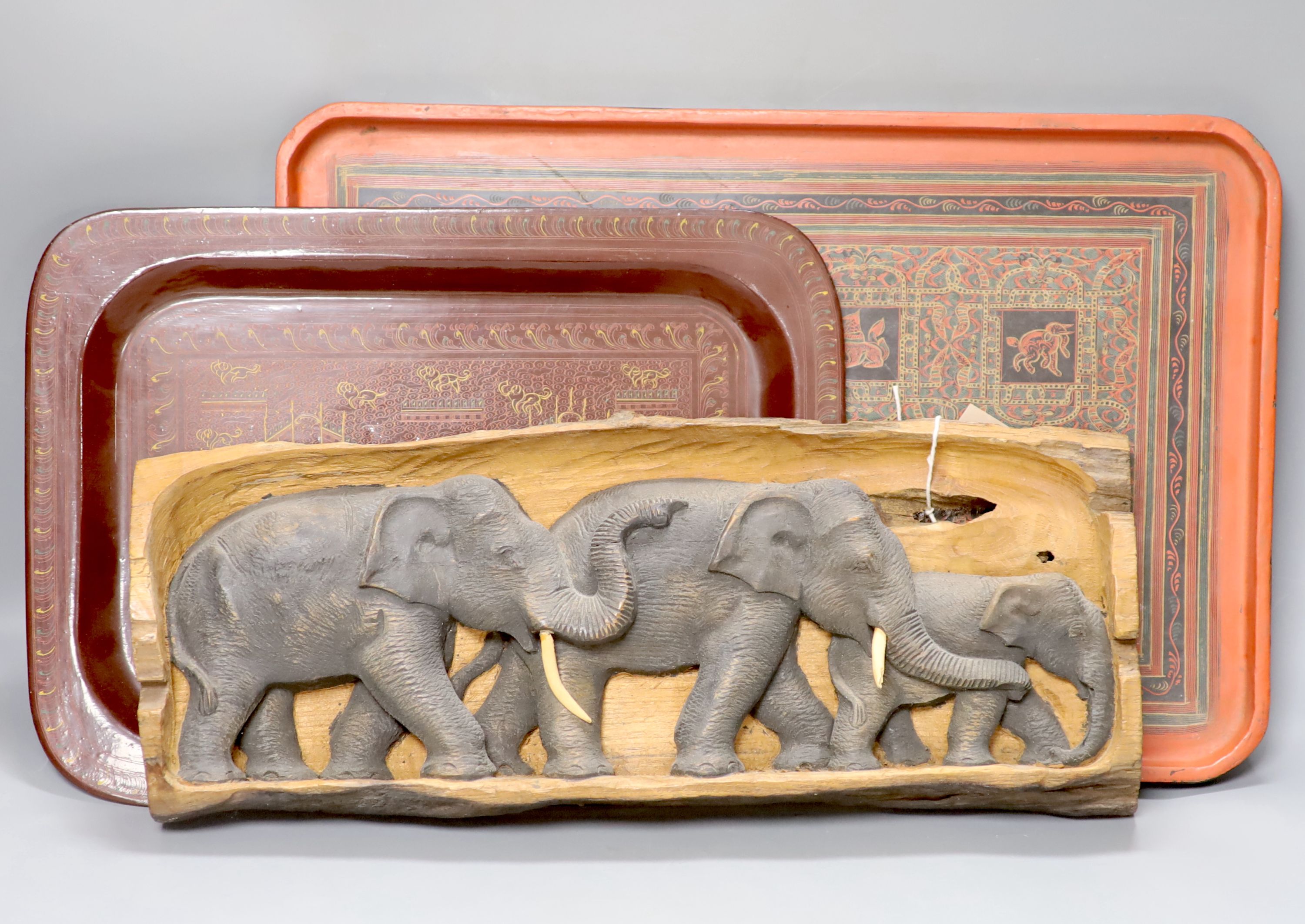 An African hardwood carving of a herd of elephants, and two papier mache trays, largest 46cm